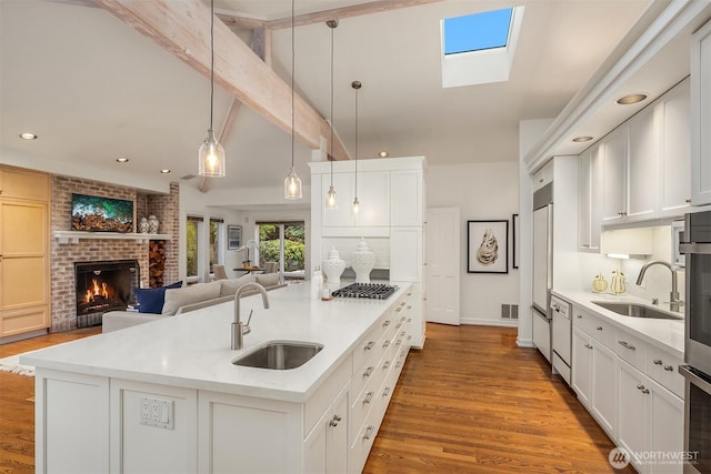 kitchen with a center island with sink, a sink, wood finished floors, a brick fireplace, and stainless steel gas cooktop