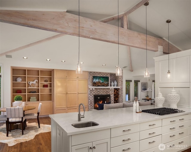 kitchen featuring a sink, lofted ceiling with beams, stainless steel gas stovetop, light countertops, and dark wood-style flooring