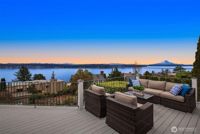 deck at dusk with an outdoor living space and a water view