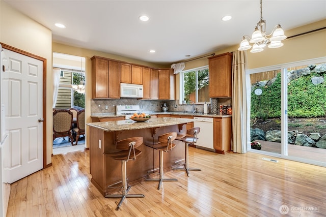 kitchen with light wood-type flooring, decorative backsplash, white appliances, and an inviting chandelier