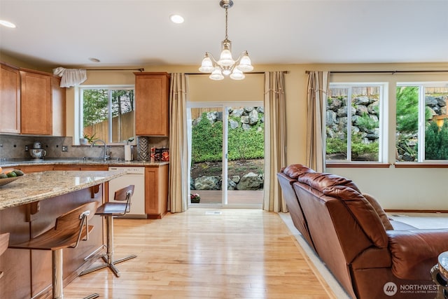 kitchen with light wood-type flooring, decorative light fixtures, decorative backsplash, light stone countertops, and dishwasher