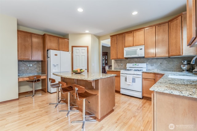 kitchen featuring light stone counters, white appliances, light wood-type flooring, and a sink