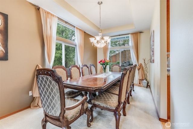 dining area featuring a tray ceiling, a notable chandelier, baseboards, and light carpet