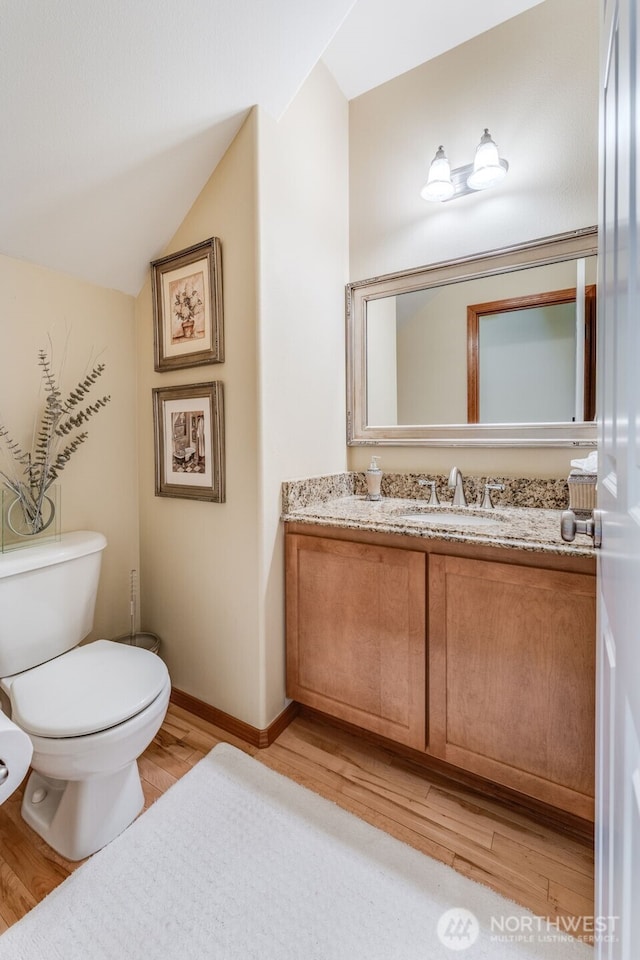 bathroom with vanity, wood finished floors, baseboards, lofted ceiling, and toilet