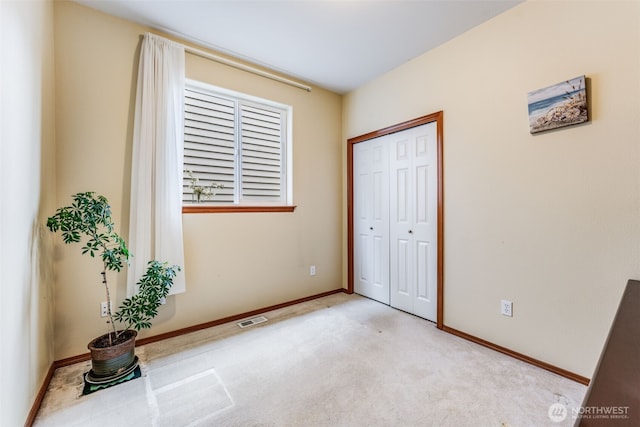 unfurnished bedroom featuring a closet, baseboards, light colored carpet, and visible vents