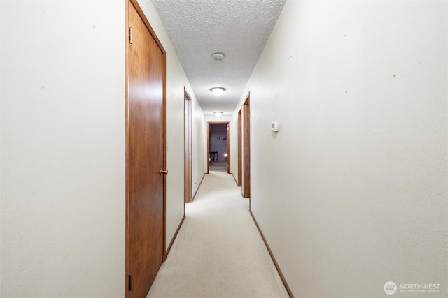 hall featuring light colored carpet, baseboards, and a textured ceiling