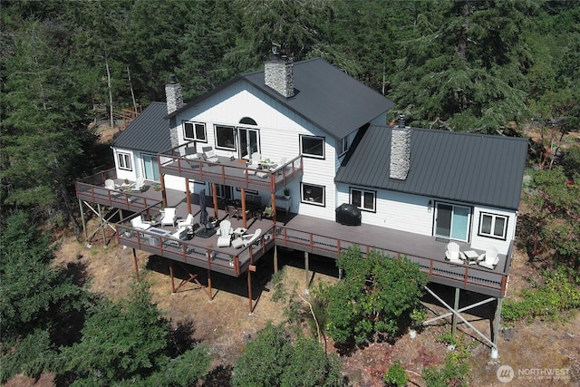back of house featuring a wooden deck, a chimney, a standing seam roof, and metal roof