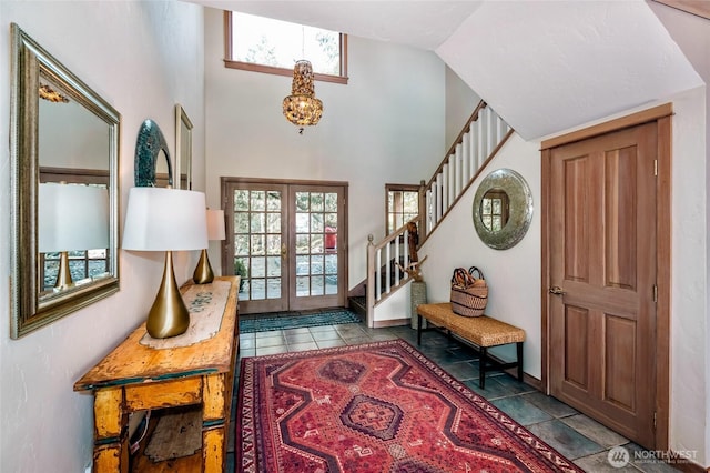 tiled entryway with french doors, a towering ceiling, baseboards, a chandelier, and stairway