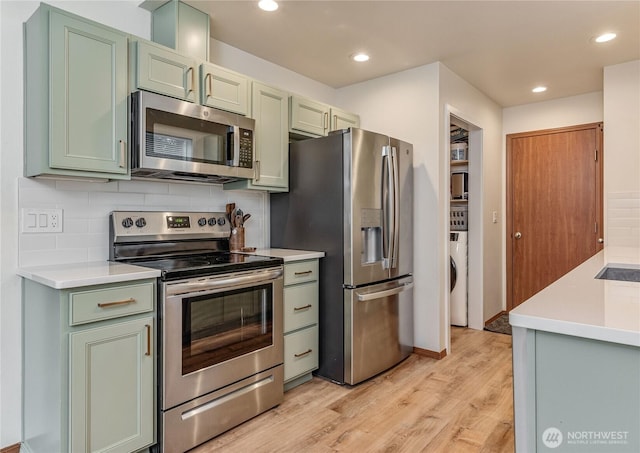 kitchen with light wood-style flooring, decorative backsplash, green cabinets, and stainless steel appliances