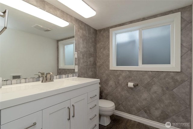 bathroom featuring vanity, wood finished floors, visible vents, tile walls, and toilet