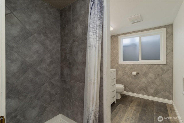 bathroom featuring baseboards, toilet, wood finished floors, and a tile shower