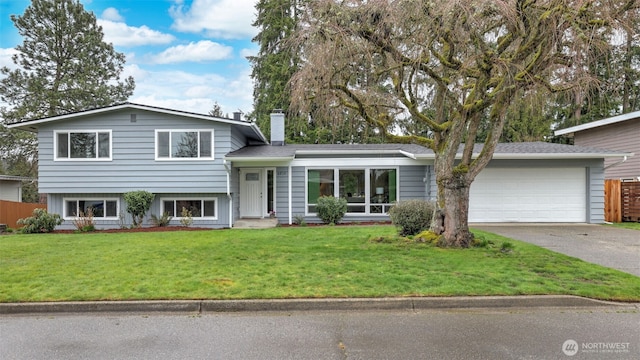 tri-level home featuring a chimney, a garage, concrete driveway, and a front yard