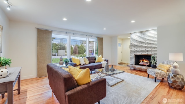 living room with recessed lighting, a brick fireplace, baseboards, and light wood-style floors