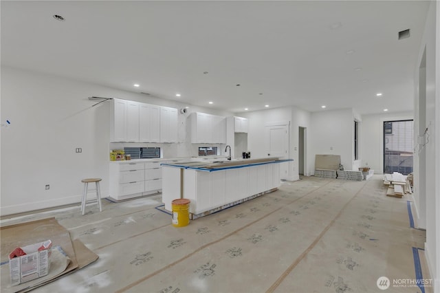 kitchen with visible vents, baseboards, a center island with sink, recessed lighting, and white cabinetry