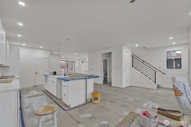 kitchen with a center island with sink, baseboards, recessed lighting, light countertops, and white cabinets