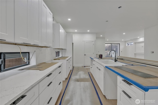 kitchen with a sink, light stone countertops, white cabinets, and recessed lighting