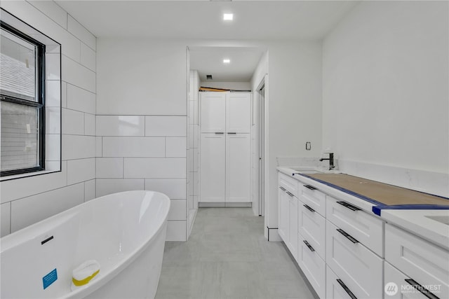 bathroom with a sink, a soaking tub, tile walls, and double vanity