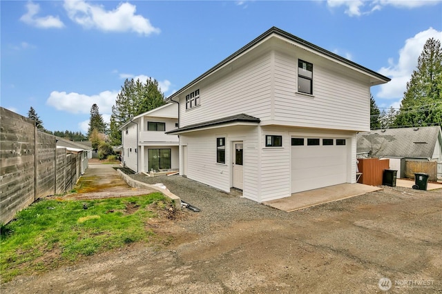 rear view of house featuring a garage, dirt driveway, and fence