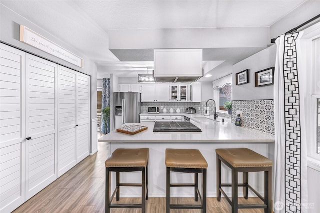 kitchen with a sink, backsplash, stainless steel fridge, a peninsula, and glass insert cabinets