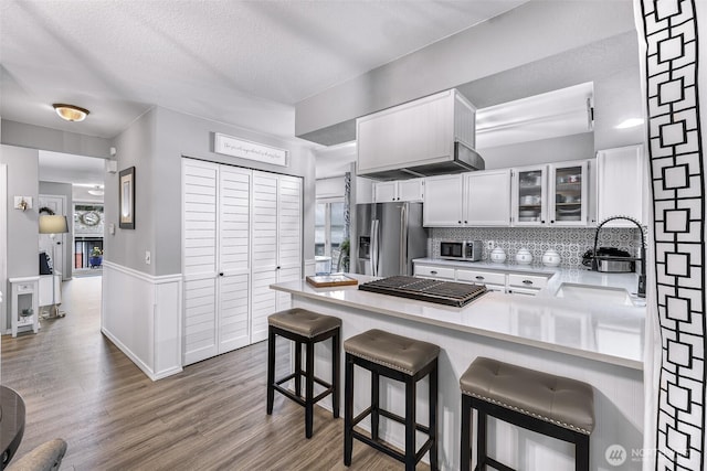 kitchen featuring wood finished floors, a peninsula, a sink, white cabinets, and appliances with stainless steel finishes