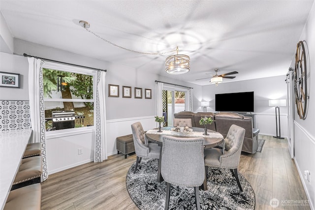 dining space with light wood-style flooring, ceiling fan with notable chandelier, baseboards, and a textured ceiling