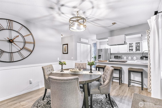 dining space with a notable chandelier, light wood-style floors, and a wainscoted wall