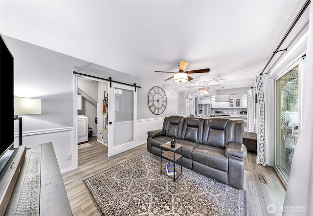 living area featuring a barn door, light wood-style flooring, visible vents, and ceiling fan