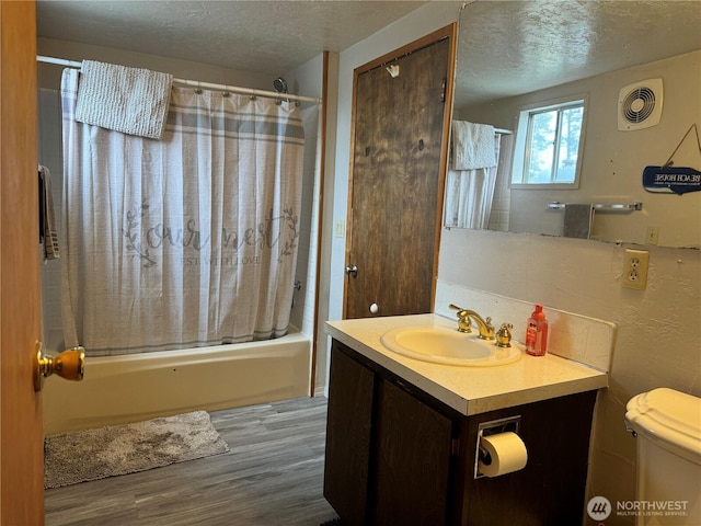 full bath featuring vanity, wood finished floors, visible vents, shower / bath combo with shower curtain, and a textured ceiling