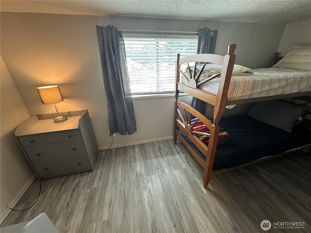 bedroom featuring baseboards, a textured ceiling, and wood finished floors