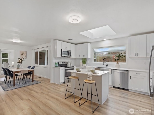 kitchen with a sink, a skylight, light wood-style floors, and stainless steel appliances