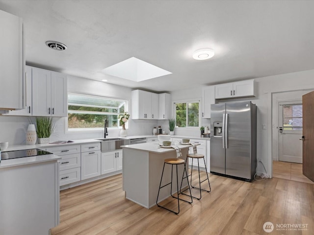 kitchen with visible vents, a skylight, stainless steel fridge with ice dispenser, a sink, and black electric stovetop