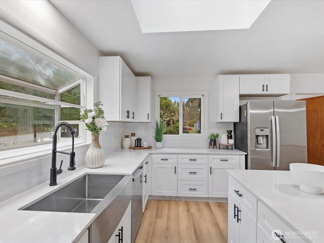 kitchen with a sink, stainless steel appliances, light wood-type flooring, and white cabinets