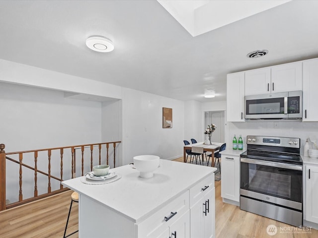 kitchen featuring light wood finished floors, visible vents, appliances with stainless steel finishes, a kitchen breakfast bar, and white cabinets