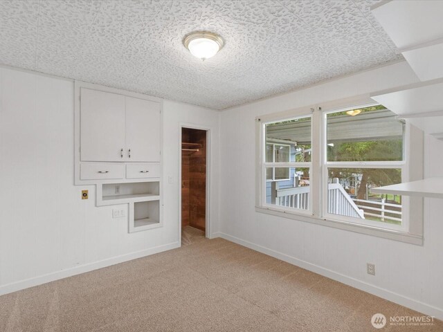 empty room featuring light carpet, a textured ceiling, and baseboards