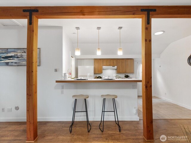 kitchen featuring hanging light fixtures, freestanding refrigerator, a breakfast bar area, and under cabinet range hood