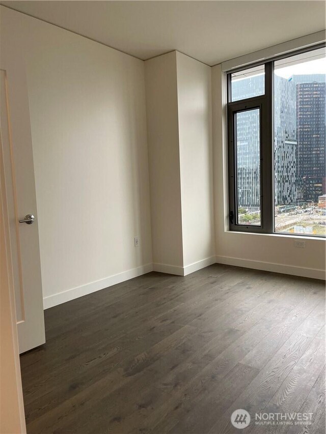 spare room featuring dark wood-style floors and baseboards