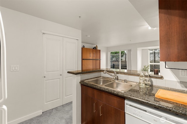 kitchen with a sink, baseboards, light colored carpet, and dishwasher