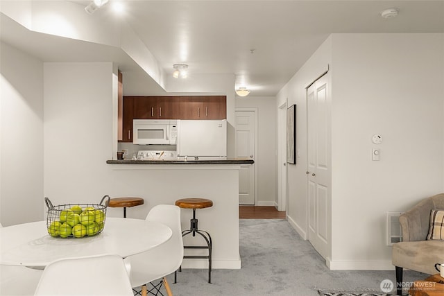 kitchen with a kitchen bar, light carpet, dark countertops, fridge, and white microwave