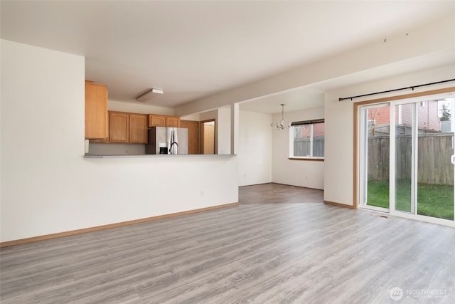 unfurnished living room with a chandelier, light wood-type flooring, and baseboards