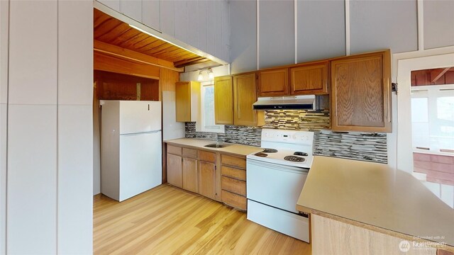 kitchen featuring light wood finished floors, under cabinet range hood, light countertops, decorative backsplash, and white appliances