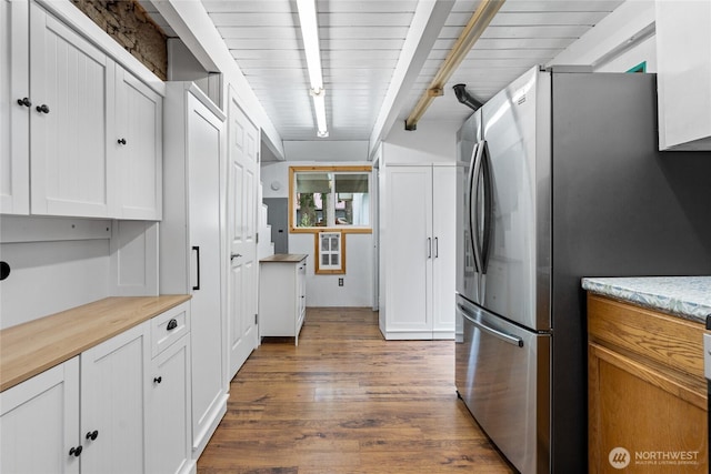 kitchen featuring wood finished floors, beam ceiling, freestanding refrigerator, butcher block countertops, and white cabinetry