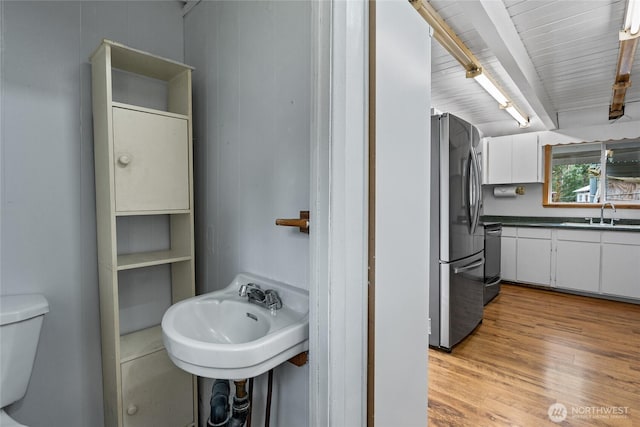 half bathroom featuring a sink, beam ceiling, toilet, and wood finished floors