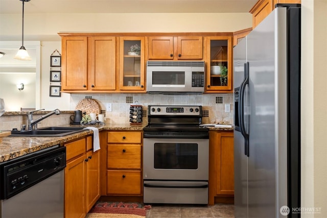 kitchen featuring tasteful backsplash, brown cabinets, stone countertops, stainless steel appliances, and a sink