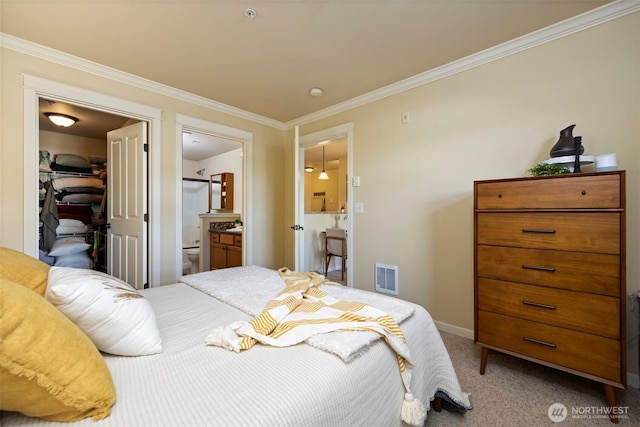 bedroom featuring visible vents, connected bathroom, crown molding, a walk in closet, and carpet flooring