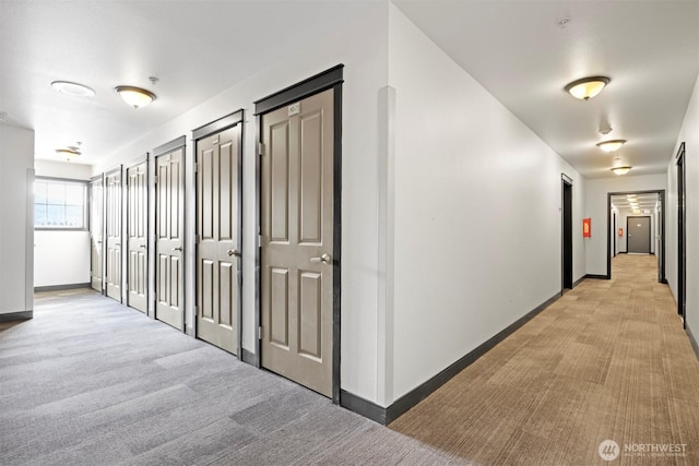 hallway with baseboards and light colored carpet