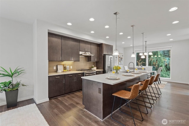 kitchen with under cabinet range hood, backsplash, stainless steel appliances, light countertops, and dark brown cabinets