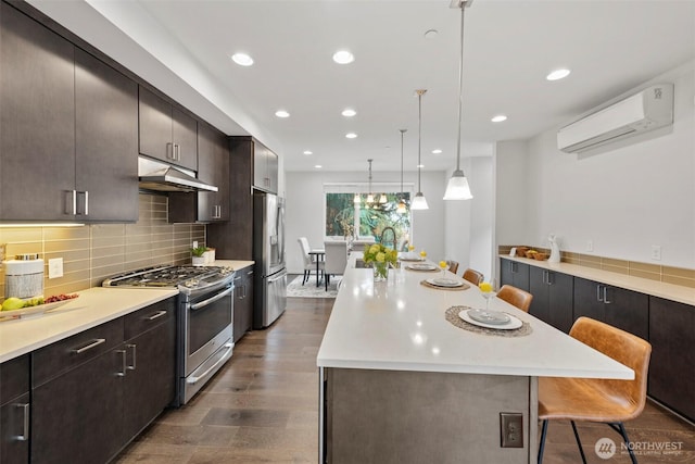 kitchen featuring under cabinet range hood, dark wood finished floors, light countertops, appliances with stainless steel finishes, and a wall mounted AC