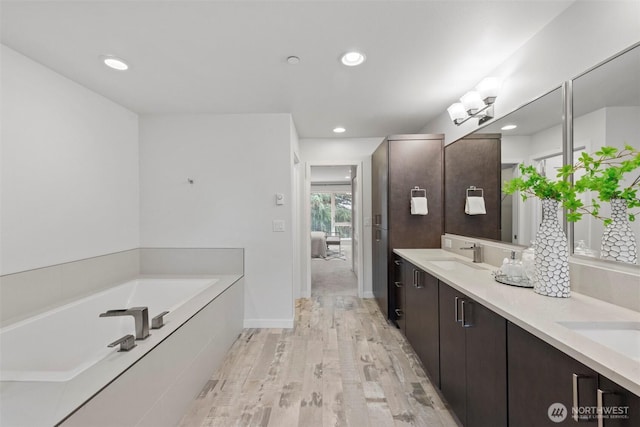 ensuite bathroom featuring double vanity, wood finished floors, a bath, ensuite bath, and a sink