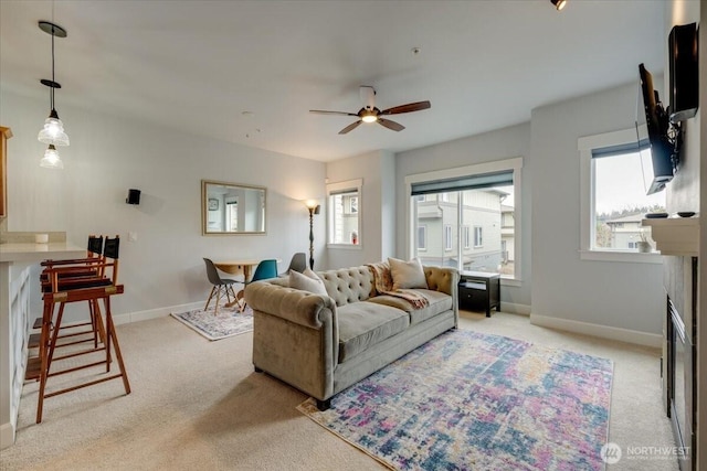 living area with ceiling fan, a fireplace, baseboards, and light carpet