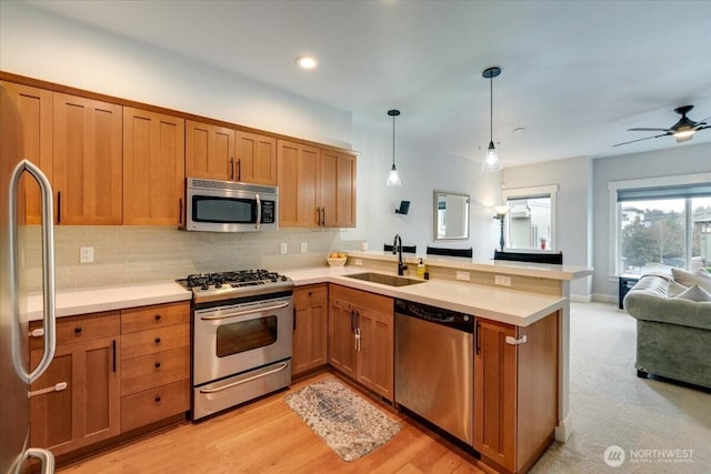 kitchen with brown cabinets, a sink, open floor plan, a peninsula, and appliances with stainless steel finishes